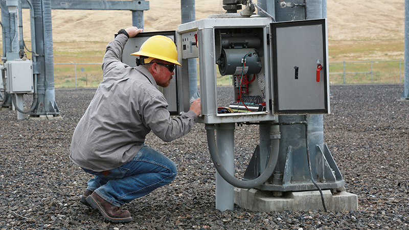 Man wearing yellow hard hat crouching to the left of an electrical box