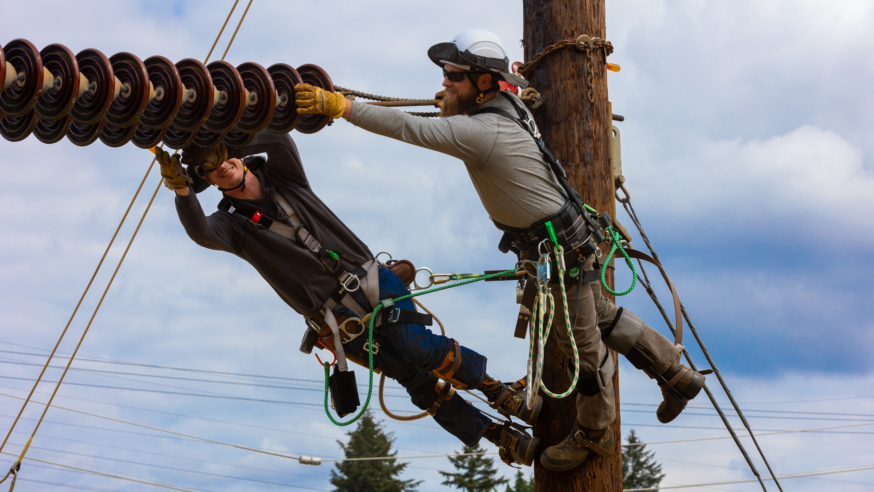 two men hanging off of electrical equipment with safety gear