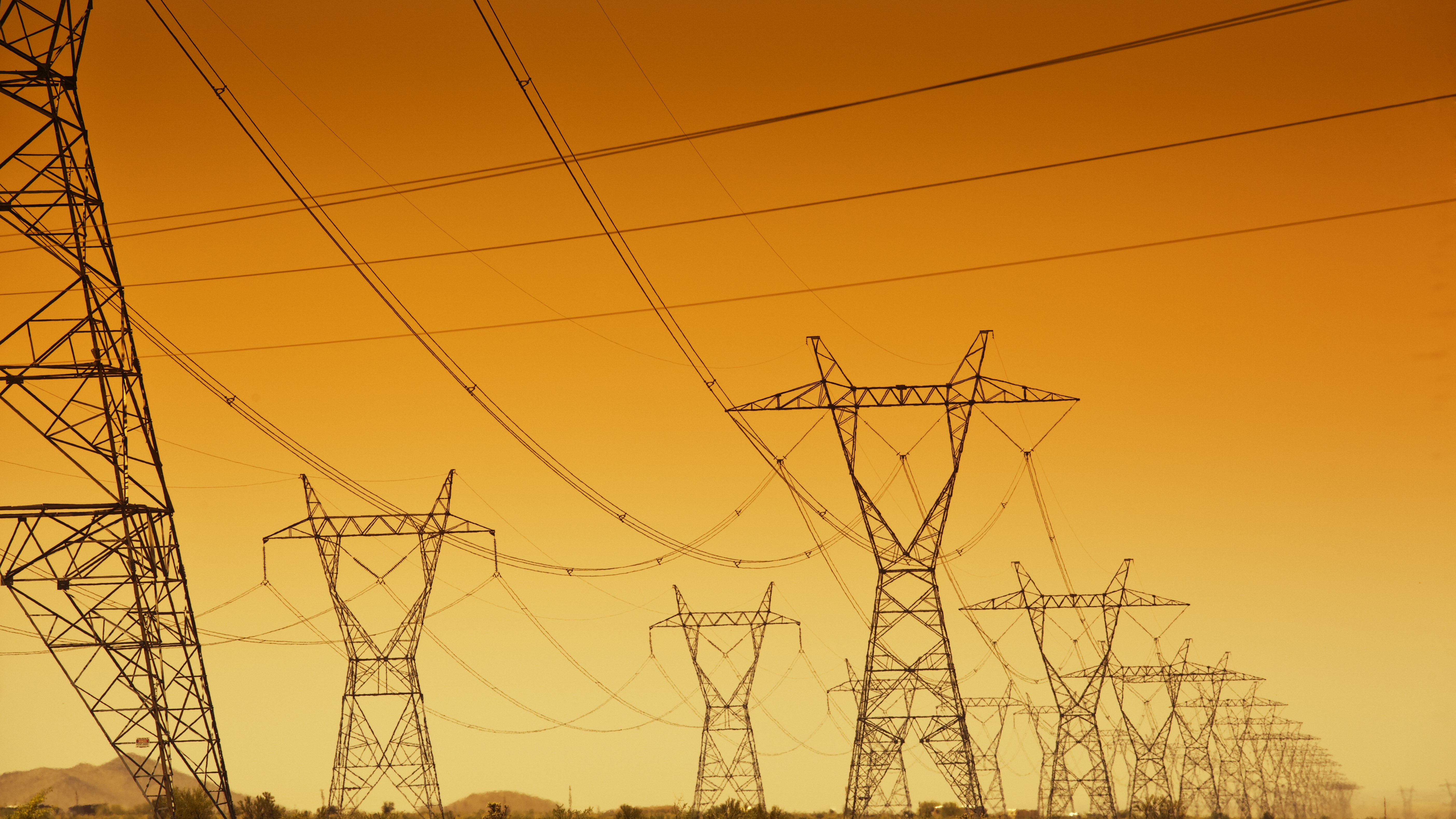 black transmission towers set against an orange and yellow sky