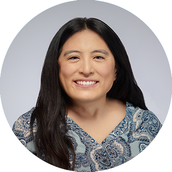 picture of woman with long dark hair, wearing a grey patterned shirt, set against a grey background, photo in shape of circle